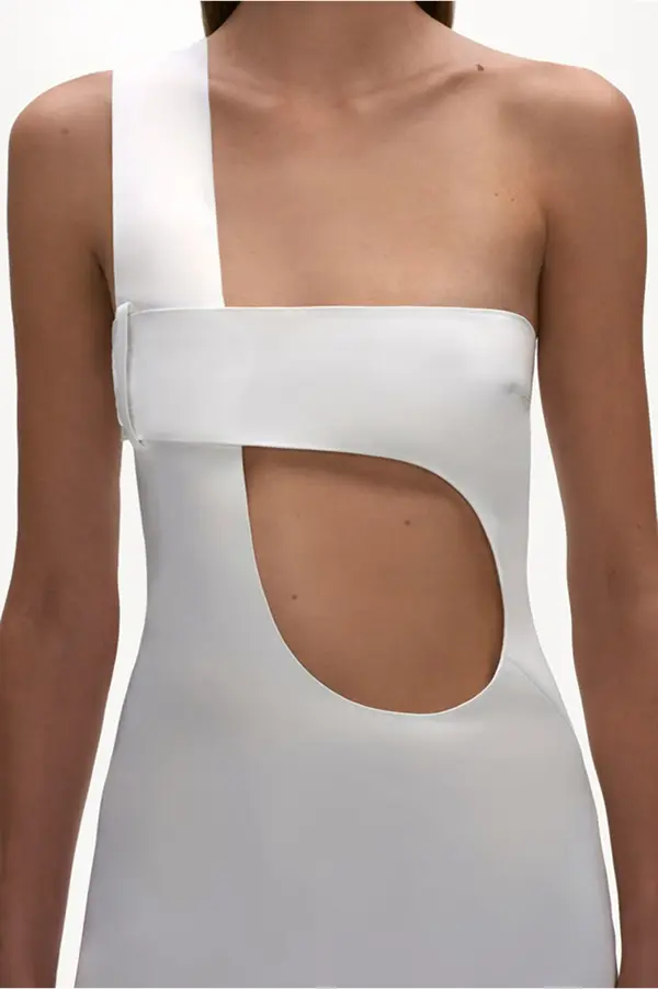 femme portant une courte robe blanche asymétrique, découpe arondie asymétriqiue au niveau du ventre