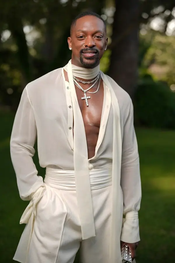 homme portant une chemise ovuerte blanche et transparente ainsi qu'un pantalon blanc